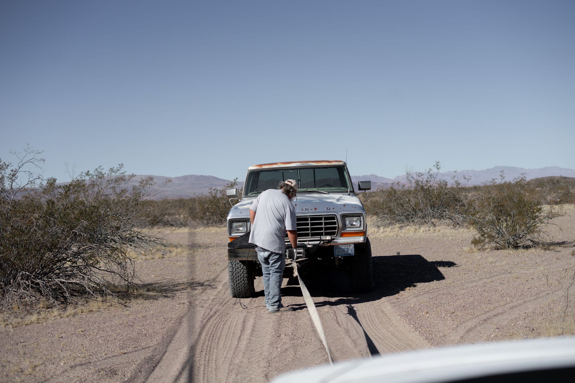 Man assisting stranded pickup truck in arid desert setting.